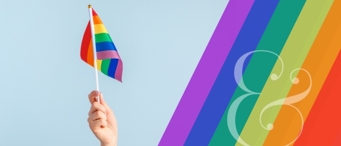 Graphic features a hand holding up a rainbow Pride flag and a rainbow design to the right of the image.