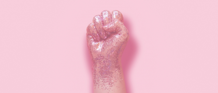 A pink, glittery fist is in front of a pale pink background.